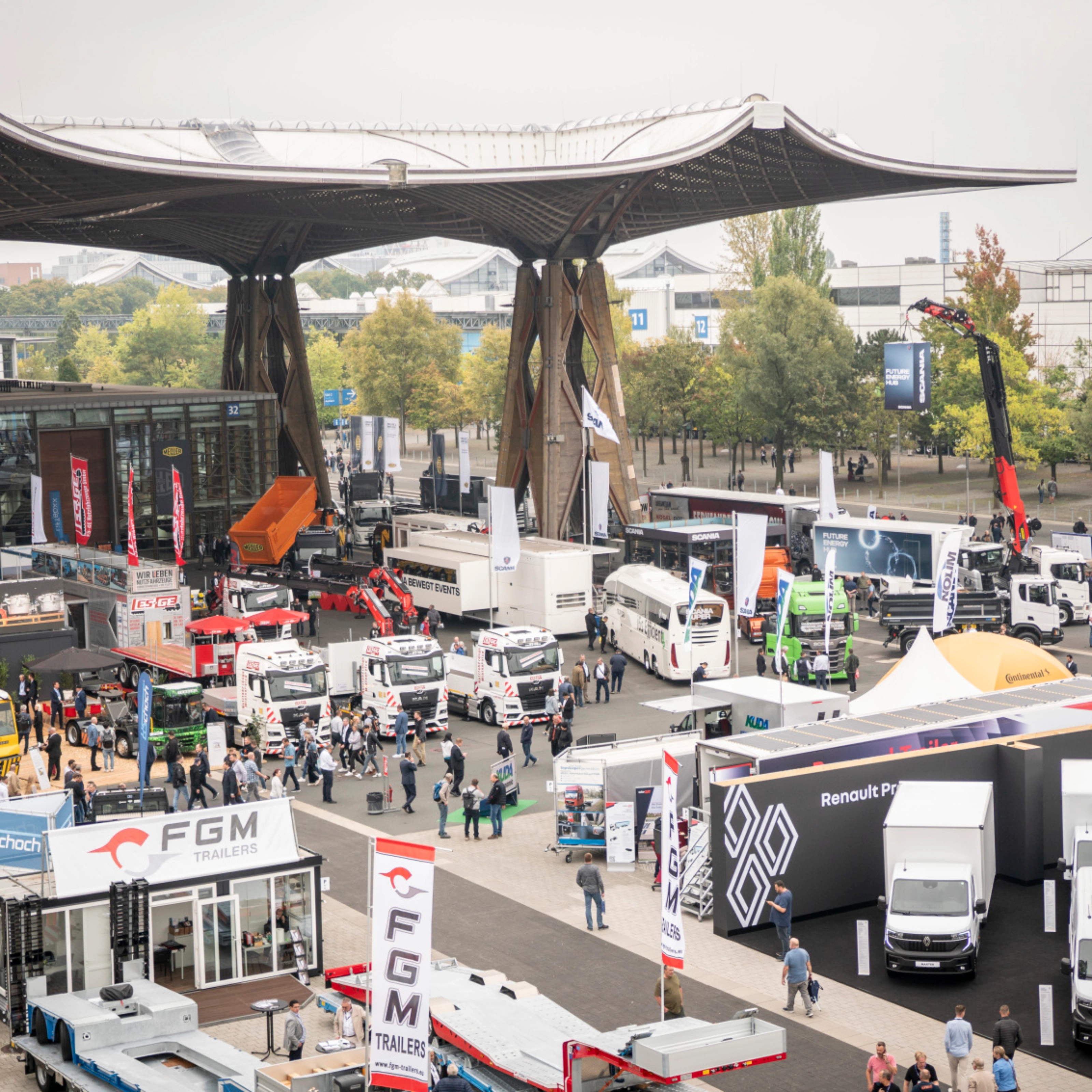 Man presenting vehicle technology on a lit-up stage at a trade fair with audience watching.