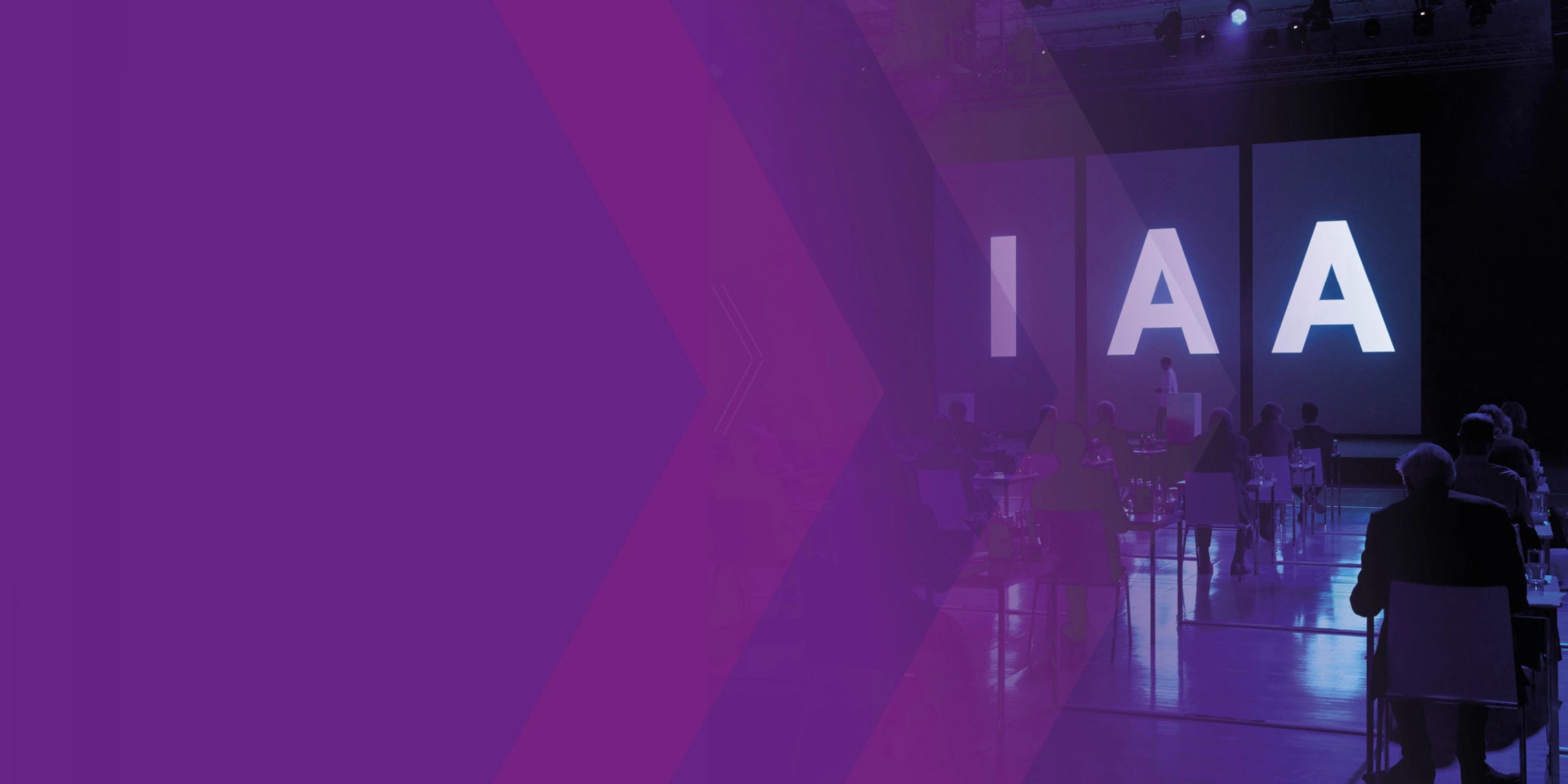 Audience seated at IAA event with large illuminated letters on stage.