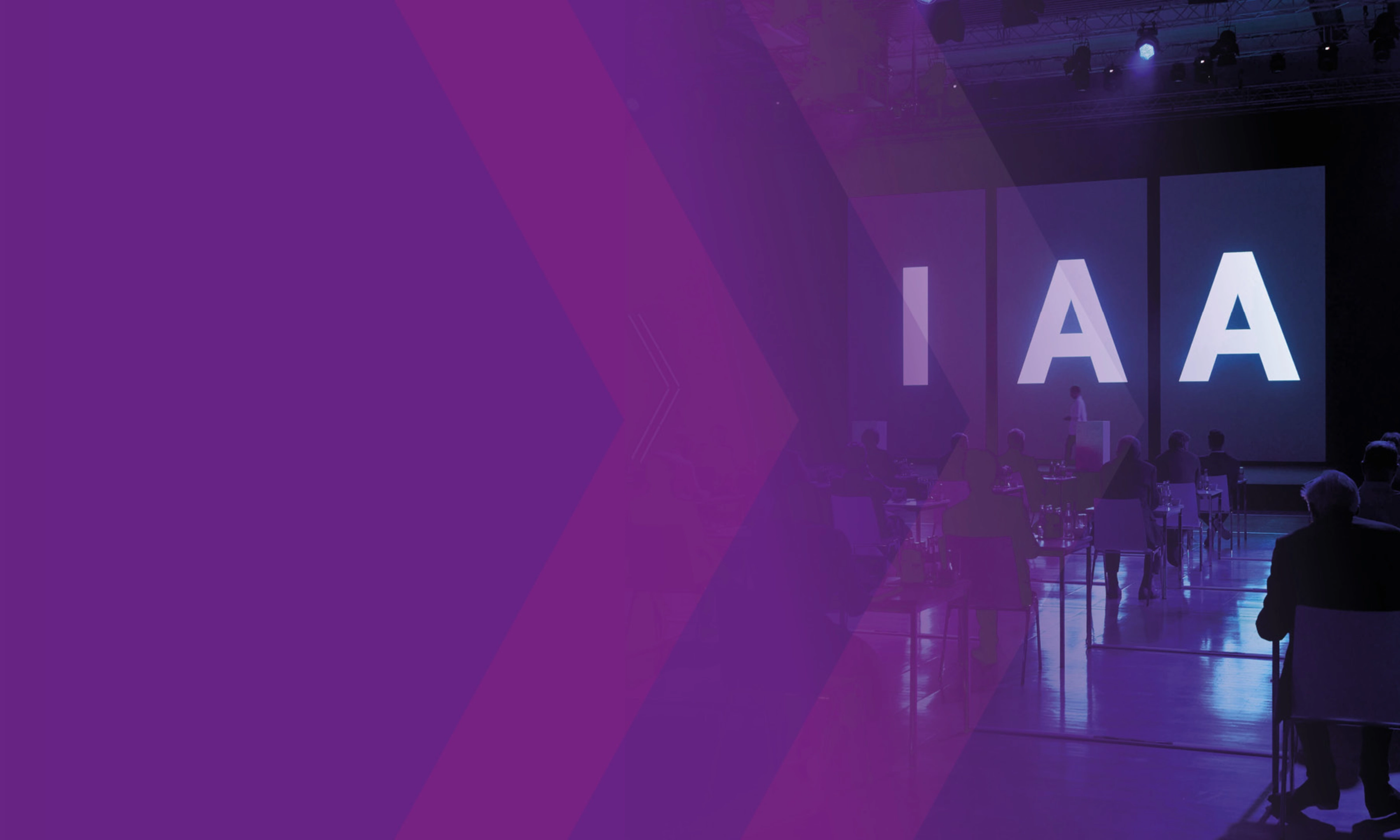 Audience seated at IAA event with large illuminated letters on stage.
