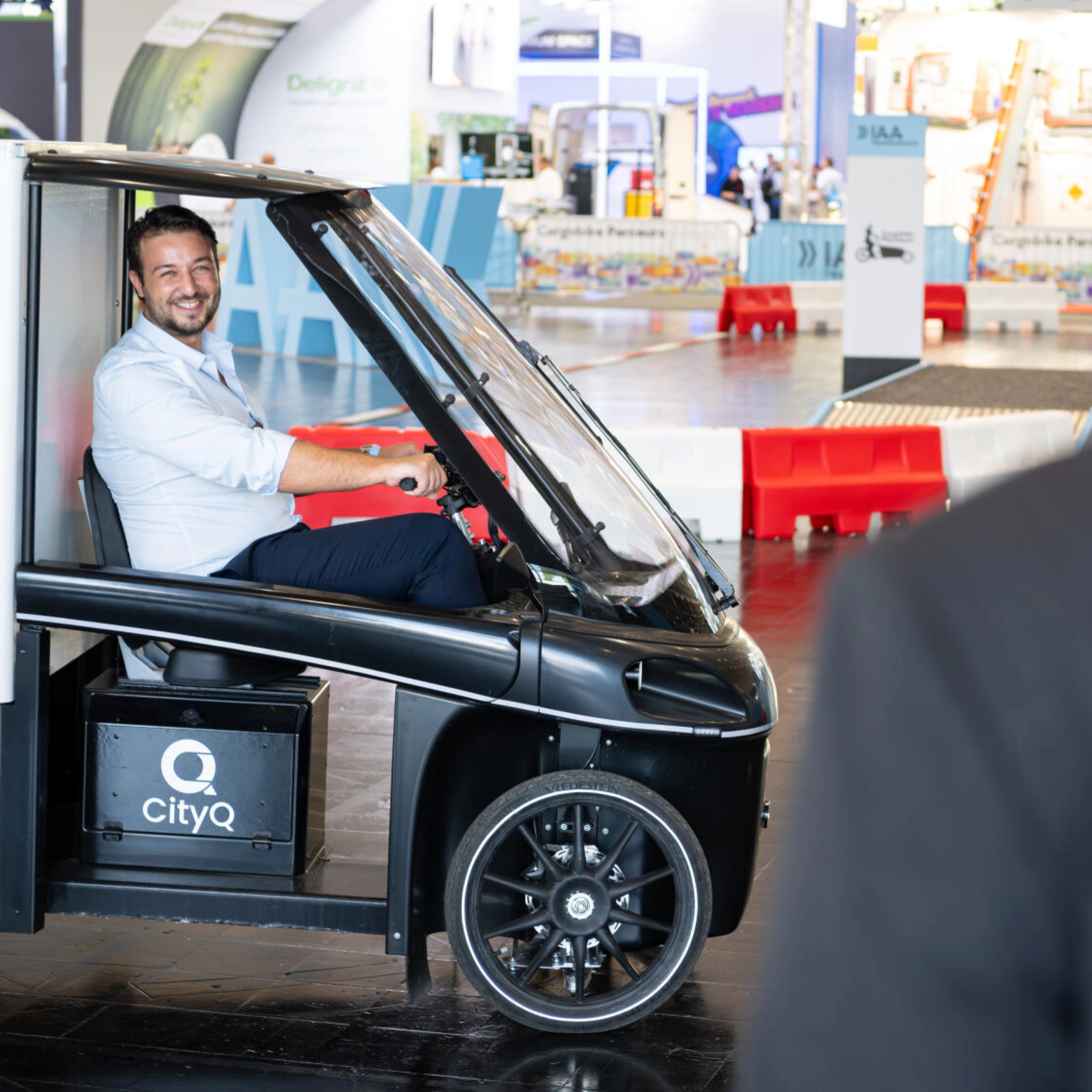Man sitting in a CityQ cargo bike inside an exhibition hall.