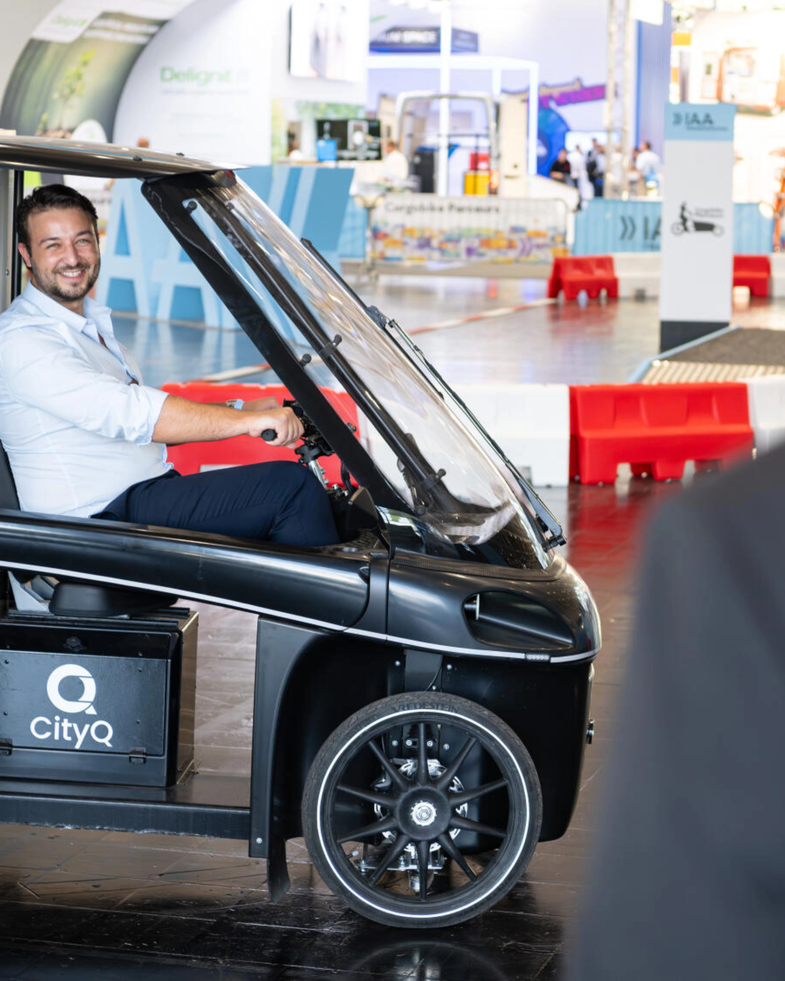 Man sitting in a CityQ cargo bike inside an exhibition hall.