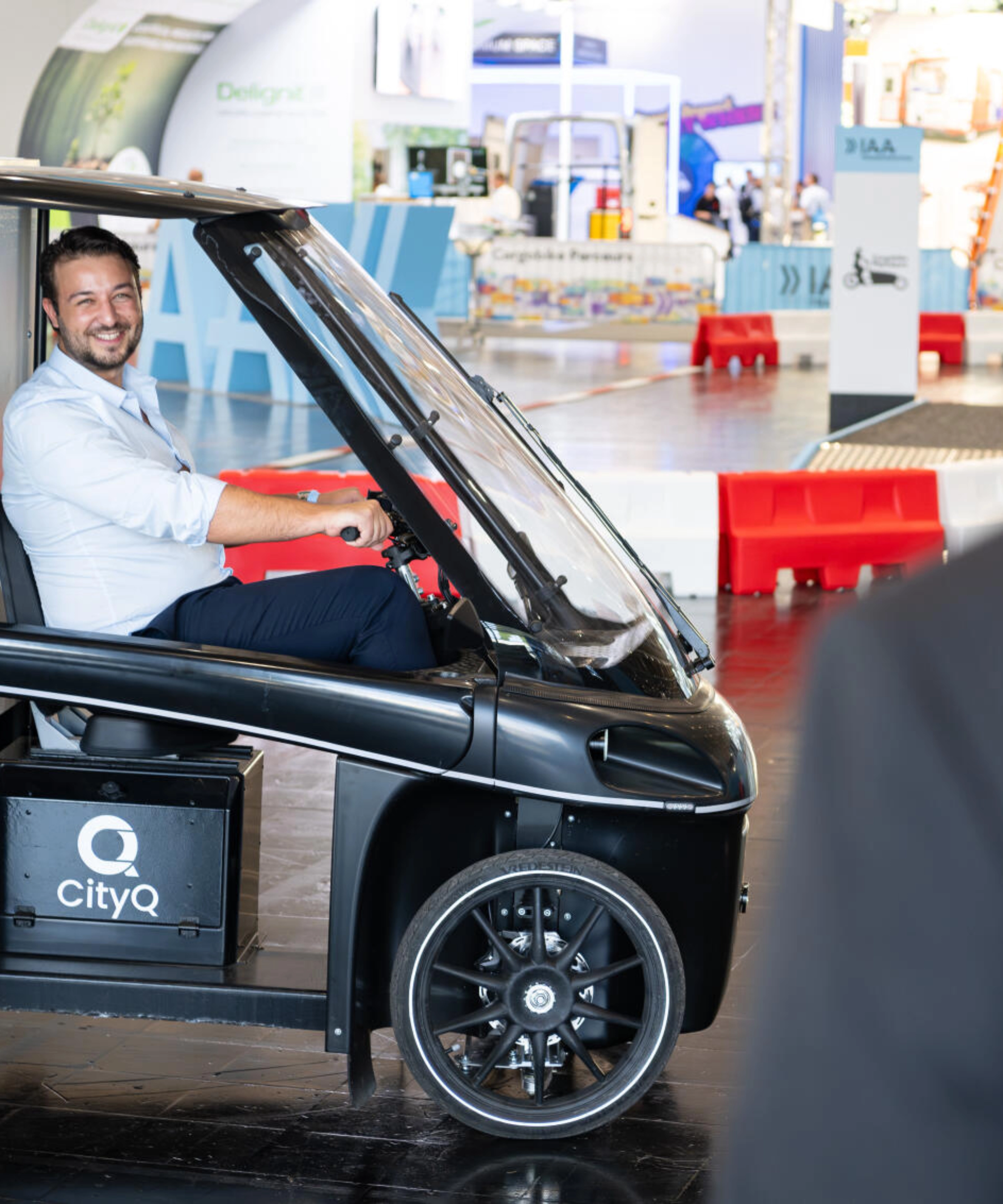 Man sitting in a CityQ cargo bike inside an exhibition hall.