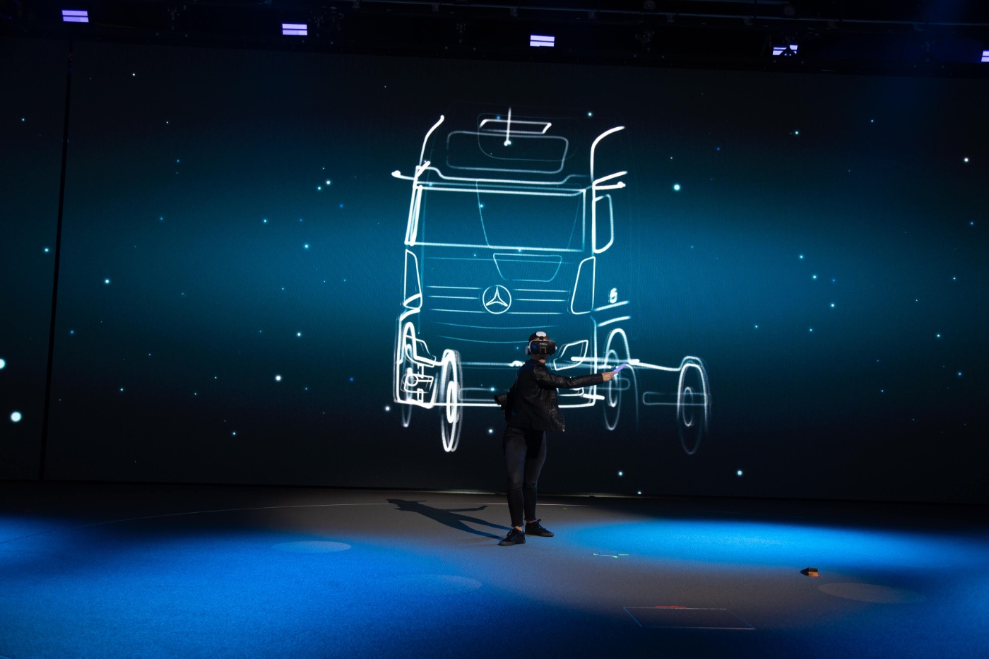 Präsentator steht vor großer Leinwand mit Umriss eines Lkw.