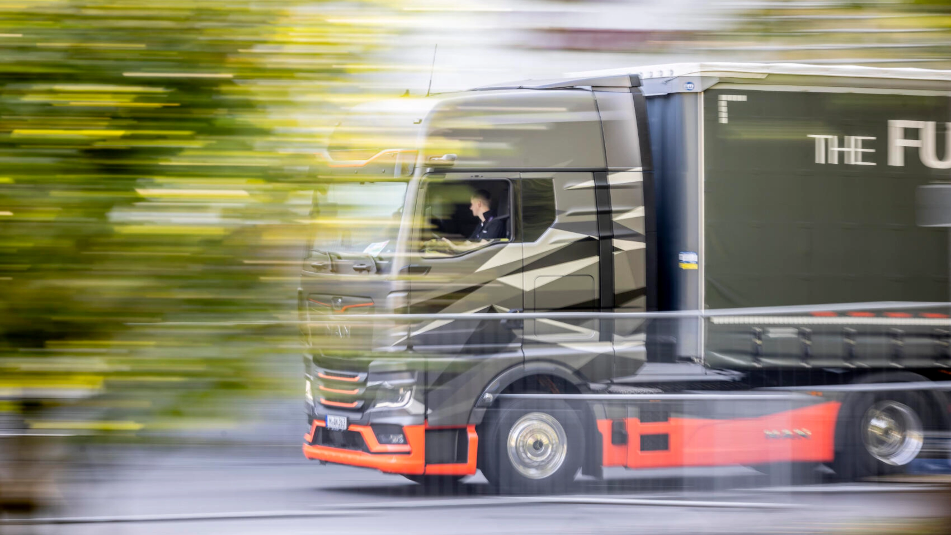 A modern truck drives past at high speed during an outdoor test drive, with motion blur visible.