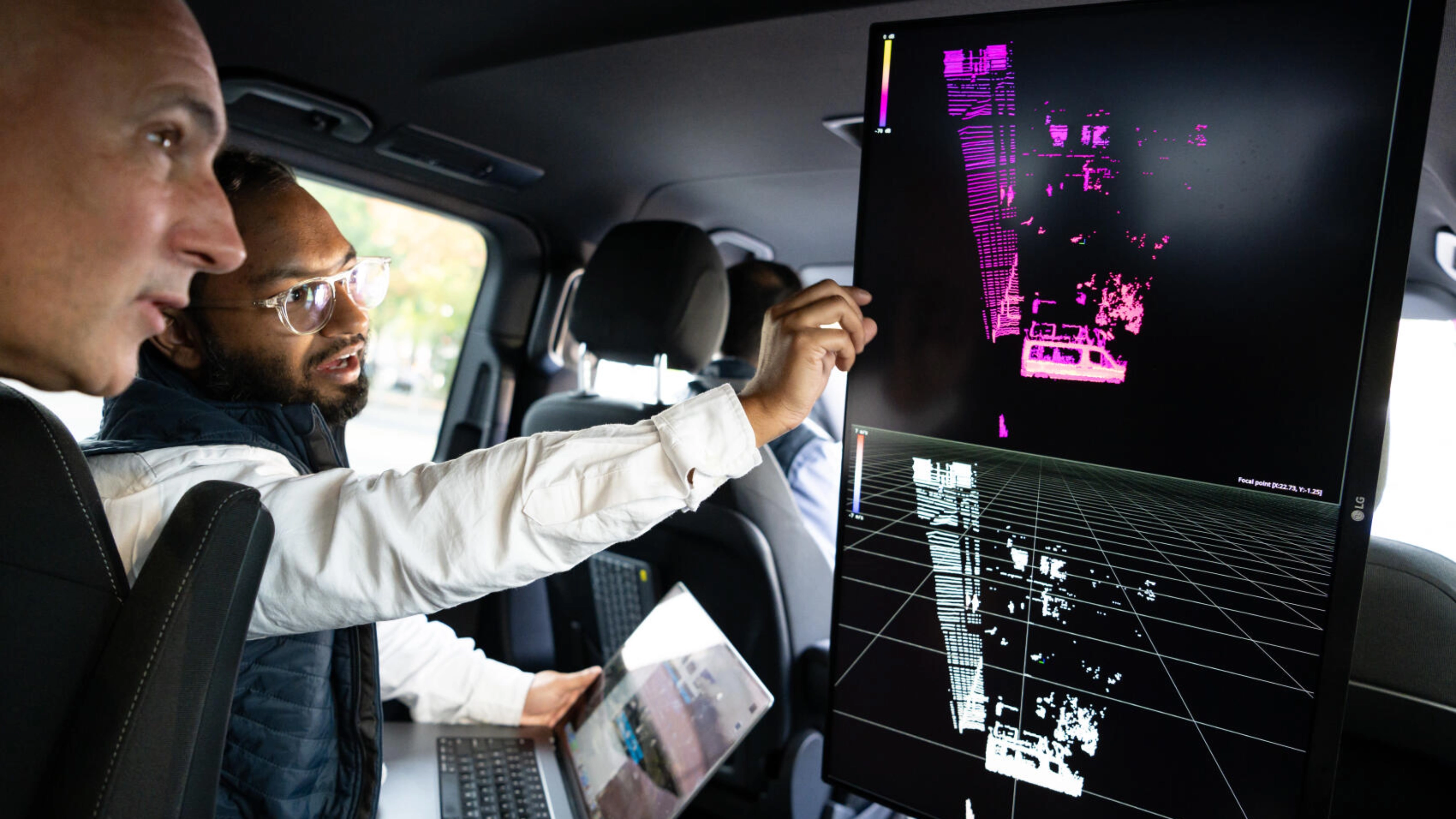 Two men analyze vehicle sensor data on a large screen inside a car